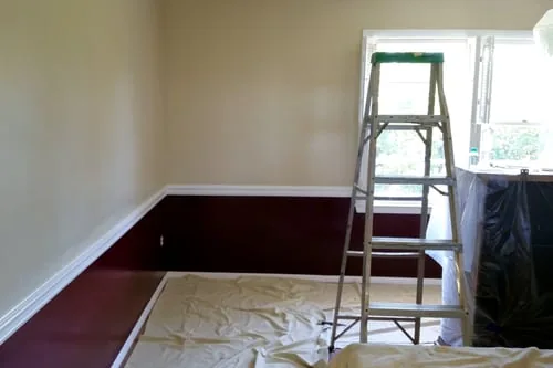 Room prepped for painting with drop cloths, a ladder, and masked trim